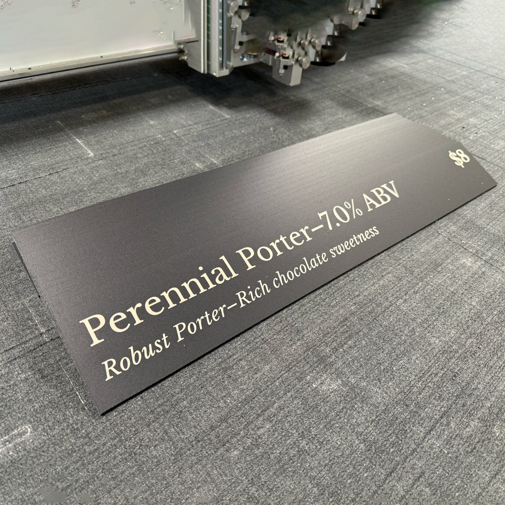 A black acrylic beer placard displaying the name 'Perennial Porter' and its ABV percentage, placed on a counter.