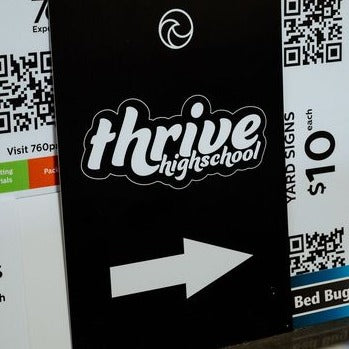 Black coroplast sign with custom print of 'thrive highschool' and an arrow pointing right, on a background with QR codes and text.