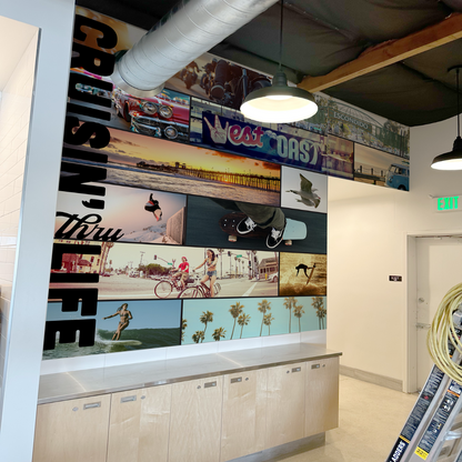 A custom vinyl wall wrap featuring various images related to surfing, installed on a wall in a room with light-colored flooring.