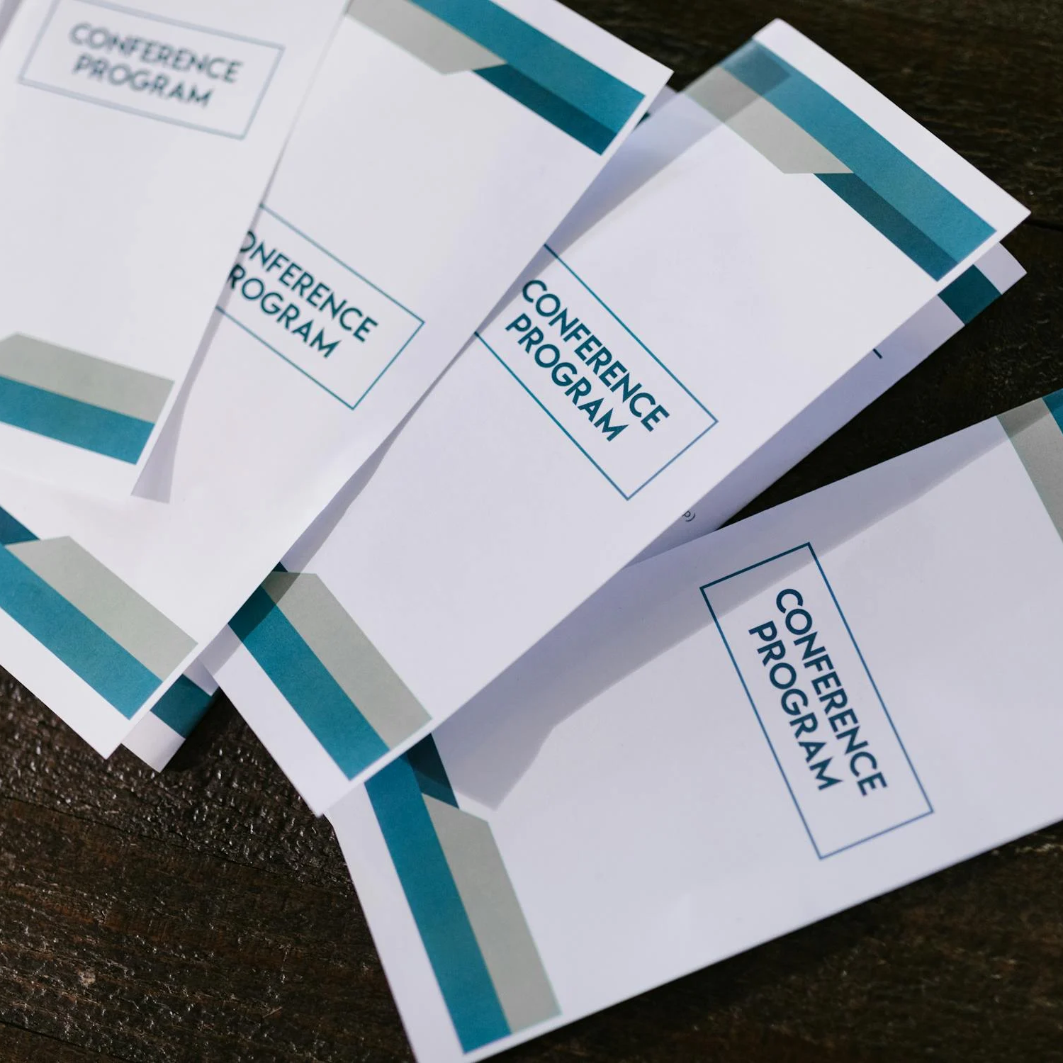 A stack of four tri-fold brochures that are being created and provided to a conference program with their colors represented on the brochures.