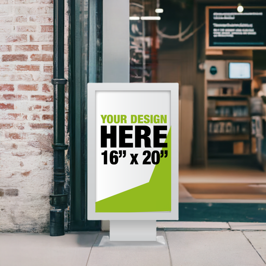 A 16 by 20 inch custom foam board mockup displayed inside a white freestanding pedestal frame placed in front of a cafe on the sidewalk, featuring placeholder text that reads Your Design Here in green and black lettering.