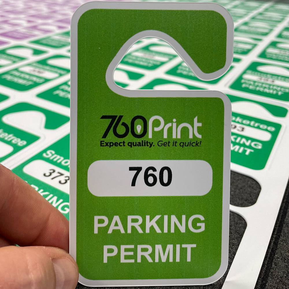A close-up of a green rear-view mirror parking permit hang tag featuring the 760 Print logo, a white box with the permit number 760, and the words PARKING PERMIT at the bottom, held next to a sheet of cut passes.