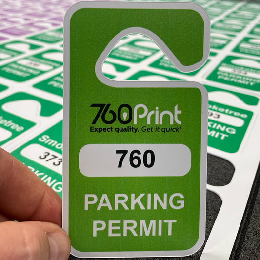 A close-up of a green rear-view mirror parking permit hang tag featuring the 760 Print logo, a white box with the permit number 760, and the words PARKING PERMIT at the bottom, held next to a sheet of cut passes.