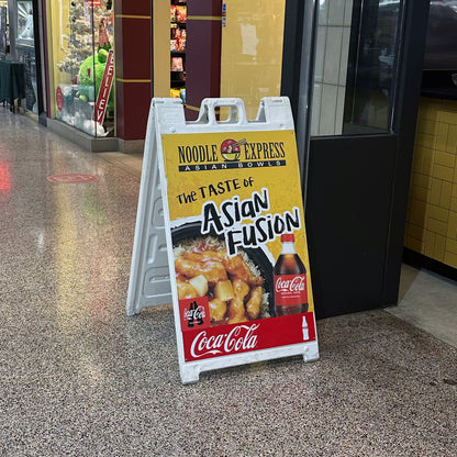 A custom printed white Plasticade A-frame sidewalk sign for Noodle Express Asian Bowls, manufactured by 760 Print and displayed in a shopping mall corridor.