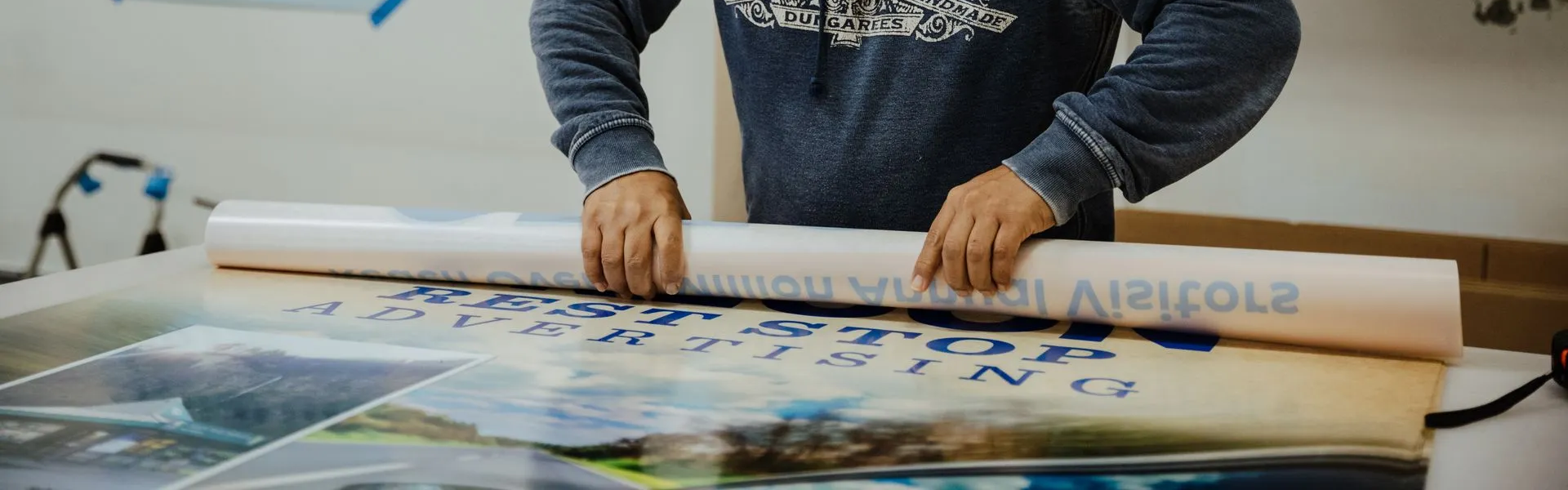 Worker rolling up high quality custom vinyl print with "REST STOP ADVERTISING" and forest setting. 