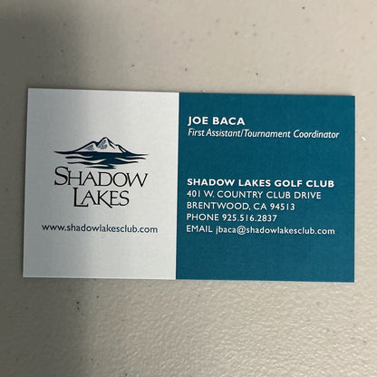 A rectangular business card for Shadow Lakes Golf Club with a split white and teal design, featuring the Shadow Lakes logo and contact information for Joe Baca, First Assistant Tournament Coordinator.