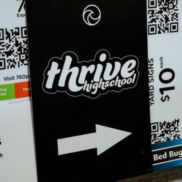 Black coroplast sign with custom print of 'thrive highschool' and an arrow pointing right, on a background with QR codes and text.