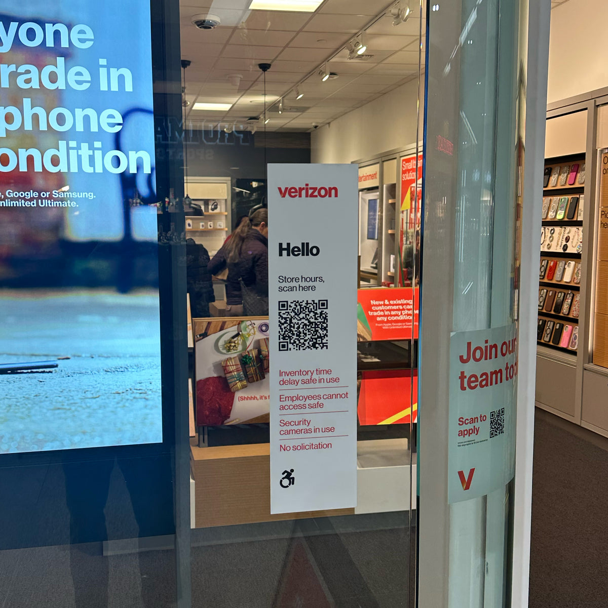 A close-up of a verizon store window display featuring a QR code for store information or joining their team, with shelves of phone protectors in the background.